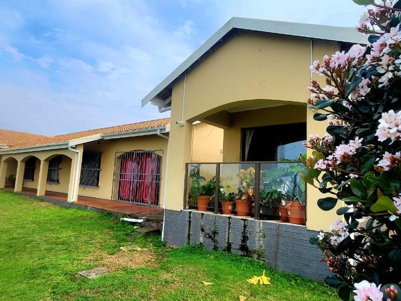 Rear view of the house featuring a covered patio with a glass balustrade, tiled roof, and access to the garden area.