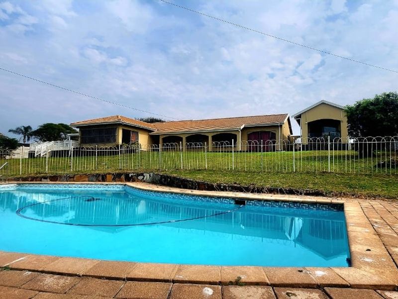 A view of the rear garden featuring a swimming pool with paved surround, overlooking the main house with a covered patio area.