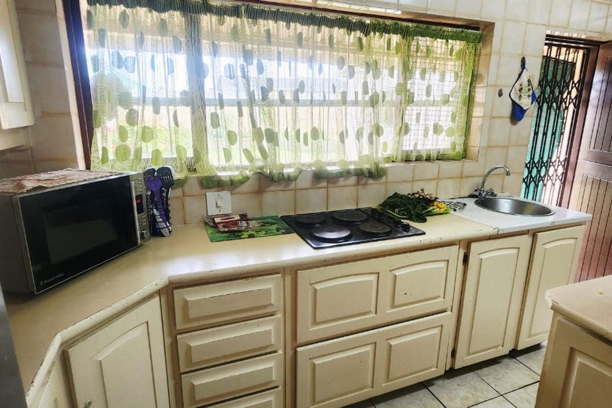 A functional kitchen featuring dated cabinetry, a tiled splashback, an electric hob, and a stainless steel sink with a window view.
