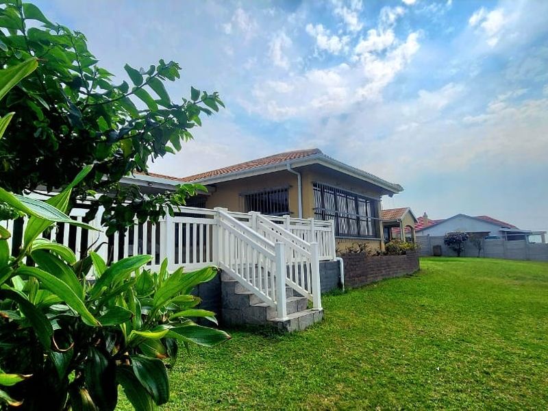 Rear view of the property featuring a raised white timber deck with stairs, a well-maintained lawn, and a brick retaining wall.
