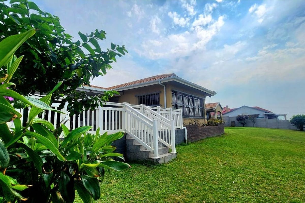 Rear view of the property featuring a raised white timber deck with stairs, a well-maintained lawn, and a brick retaining wall.