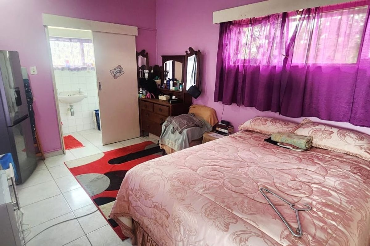 A bedroom featuring tiled flooring, a sliding door leading to an en-suite bathroom, and large windows with security bars.