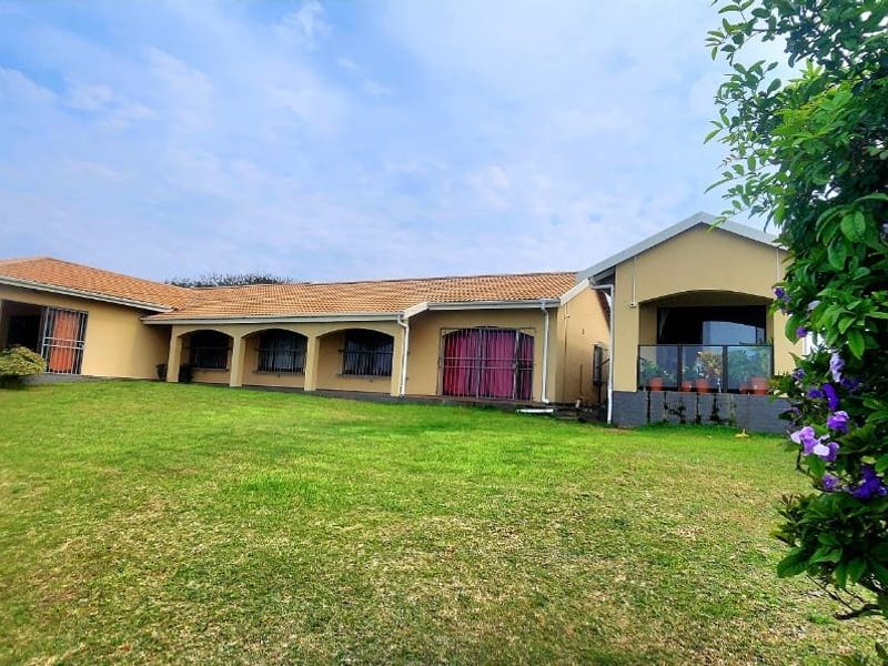 A spacious rear exterior view of the house featuring a large lawn, an arched veranda, and a raised patio area with a glass balustrade.