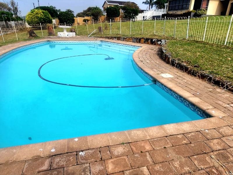 A backyard swimming pool area featuring paved surrounds, metal perimeter fencing, and a retaining wall bordering the lawn.