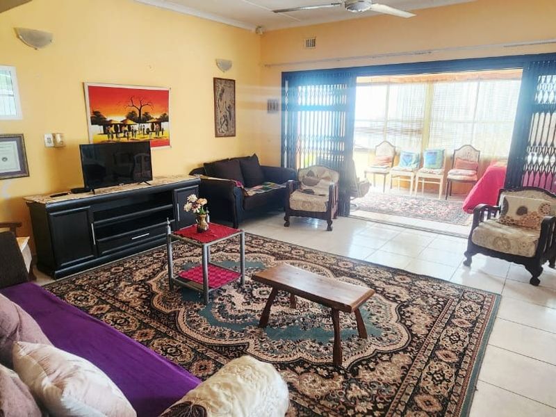 Spacious living room featuring tiled flooring, ceiling fan, and large sliding glass doors leading to an enclosed patio area with security gates.