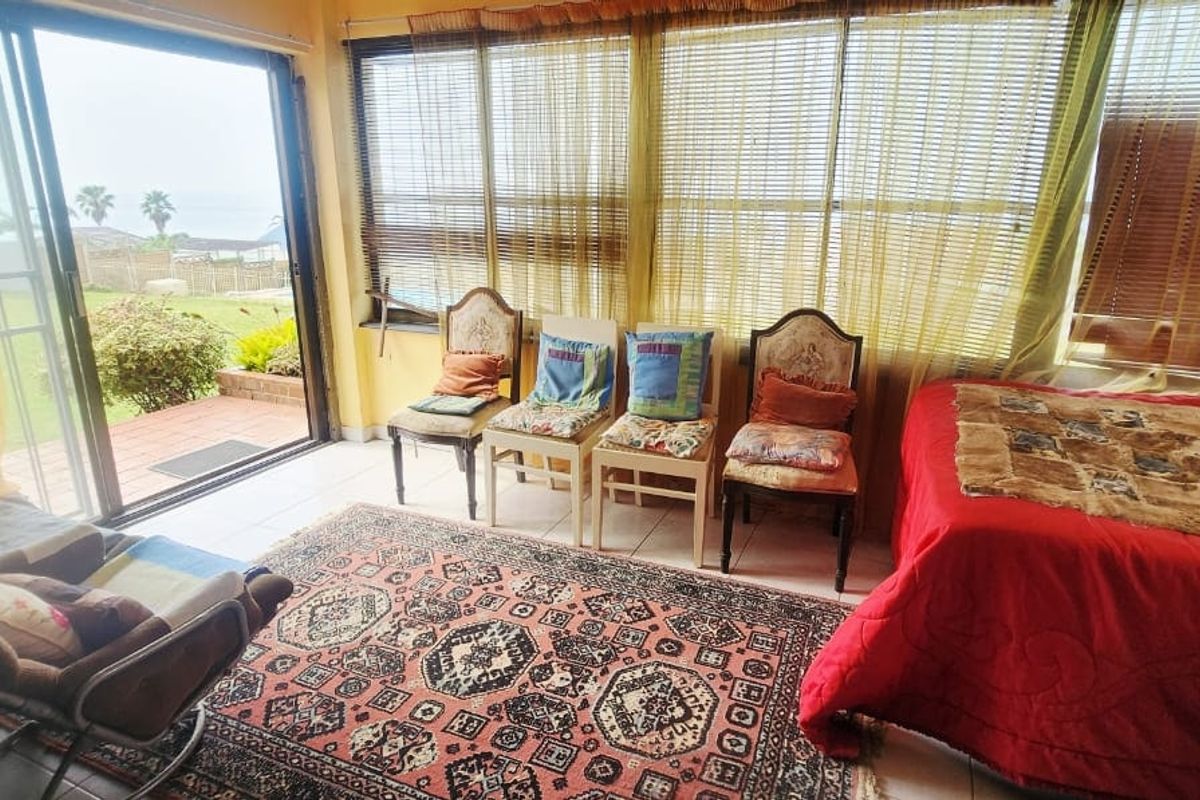 A sunlit living area featuring large windows with blinds, tiled flooring, and direct access to an outdoor patio through a sliding glass door.