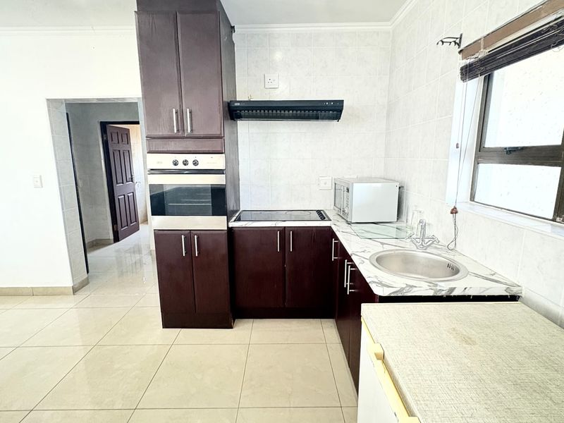 A functional kitchen featuring dark wood cabinetry, built-in oven, extractor fan, and tiled finishes, offering a practical layout for daily use.