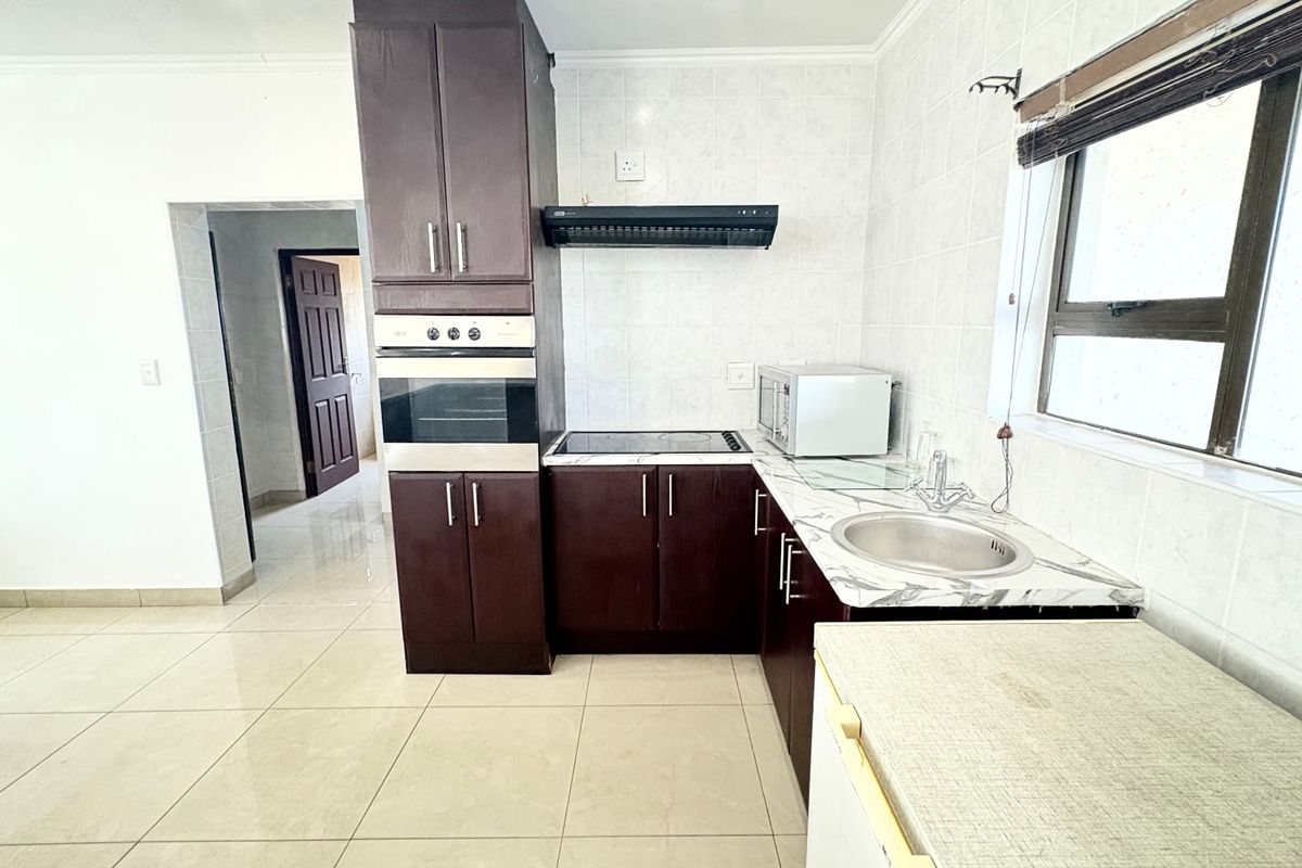 A functional kitchen featuring dark wood cabinetry, built-in oven, extractor fan, and tiled finishes, offering a practical layout for daily use.
