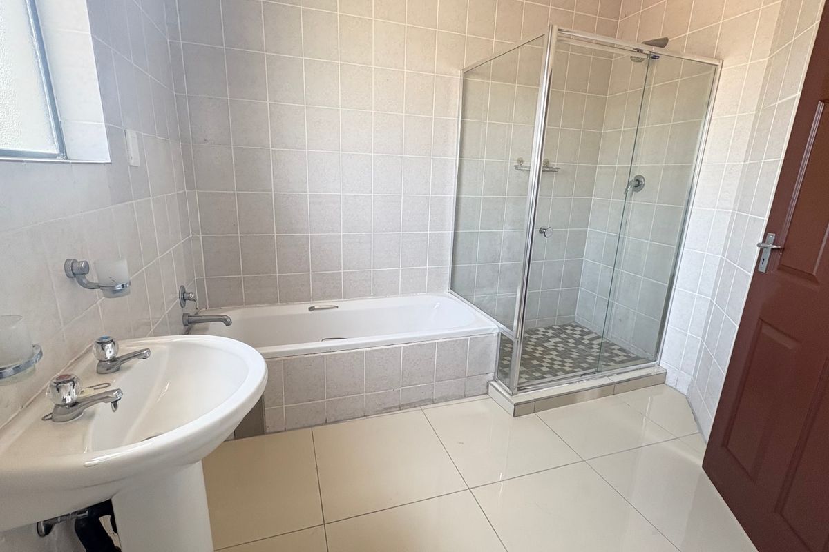 A functional bathroom featuring a pedestal basin, a built-in bathtub, and a separate glass-enclosed shower with neutral wall and floor tiling.
