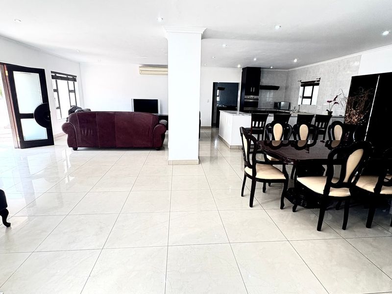 Spacious open-plan living and dining area featuring large format floor tiles, recessed lighting, and a modern kitchen with a central island.