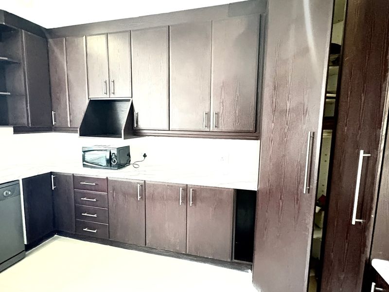A functional kitchen featuring dark wood cabinetry, stone countertops, and an integrated dishwasher, offering ample storage and a clean, modern layout.