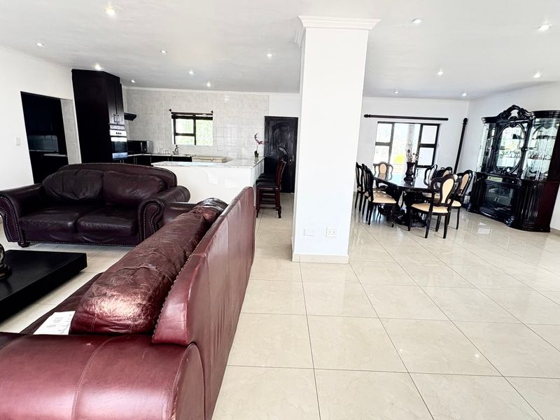 Spacious open-plan living, dining, and kitchen area featuring neutral porcelain floor tiles, recessed lighting, and a functional kitchen layout with built-in cabinetry.