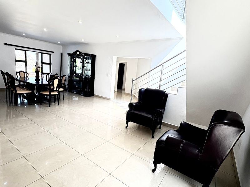 Spacious open-plan living and dining area featuring polished tile flooring, recessed lighting, and a modern staircase with a stainless steel balustrade.