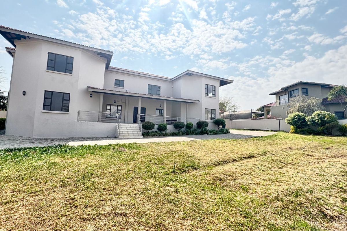 A spacious two-story residential property featuring a covered rear patio, paved driveway, and expansive lawn area.