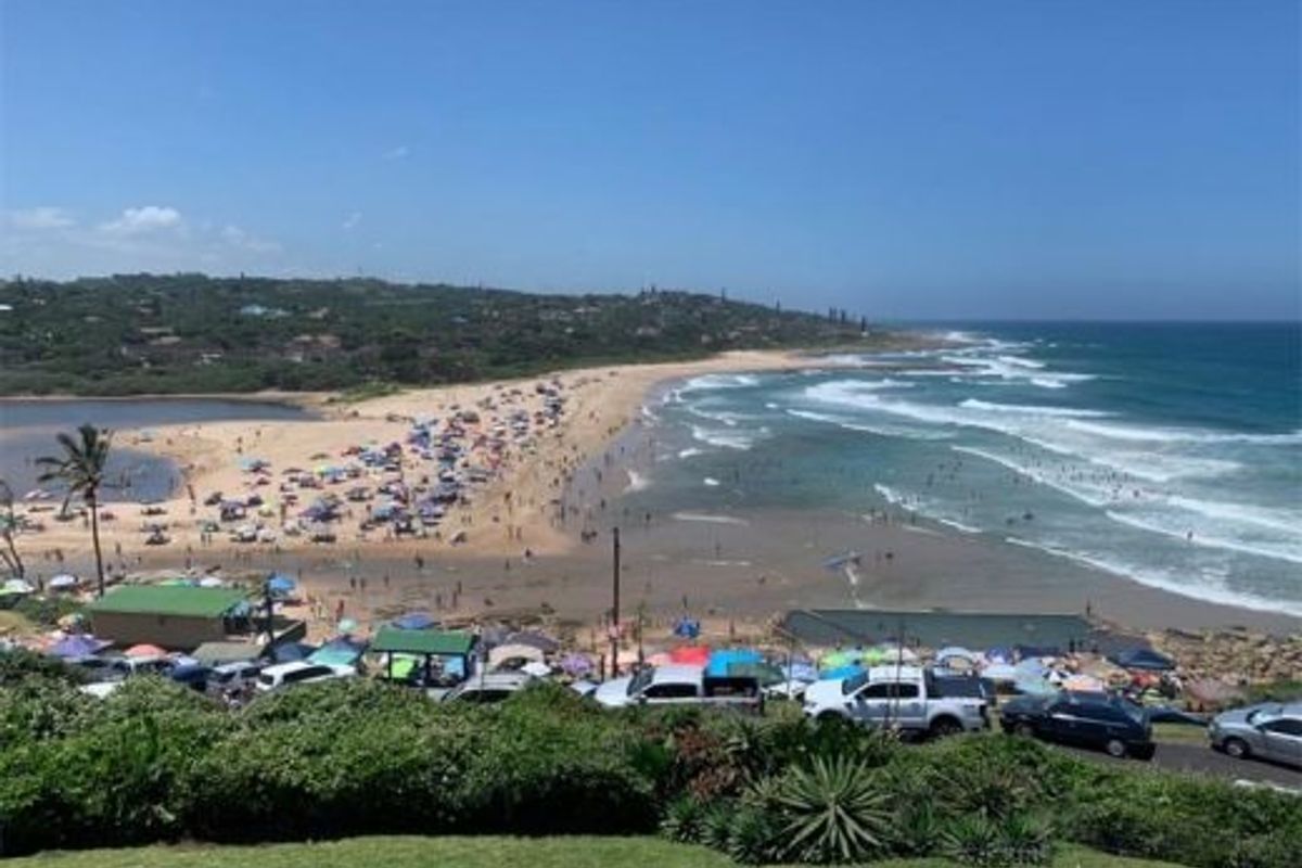 A scenic elevated view overlooking a popular coastal beach, ocean waves, and surrounding landscape.