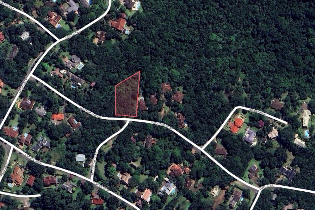 An aerial view showing a vacant residential plot surrounded by dense vegetation and established neighborhood roads.