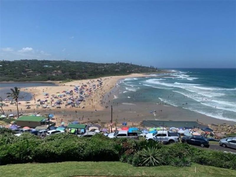 A scenic elevated view overlooking a popular coastal beach, ocean waves, and surrounding landscape.