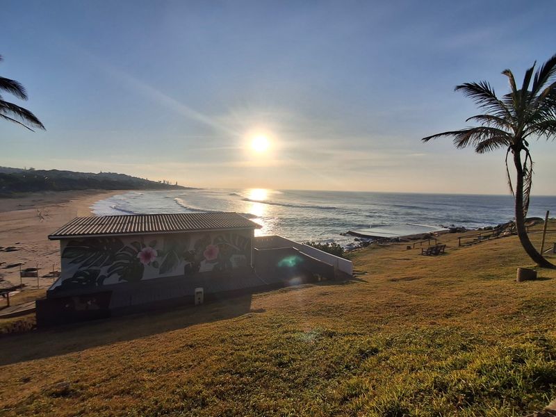 A scenic elevated view overlooking the coastline, beach, and ocean at sunset, showcasing the property's prime coastal location.