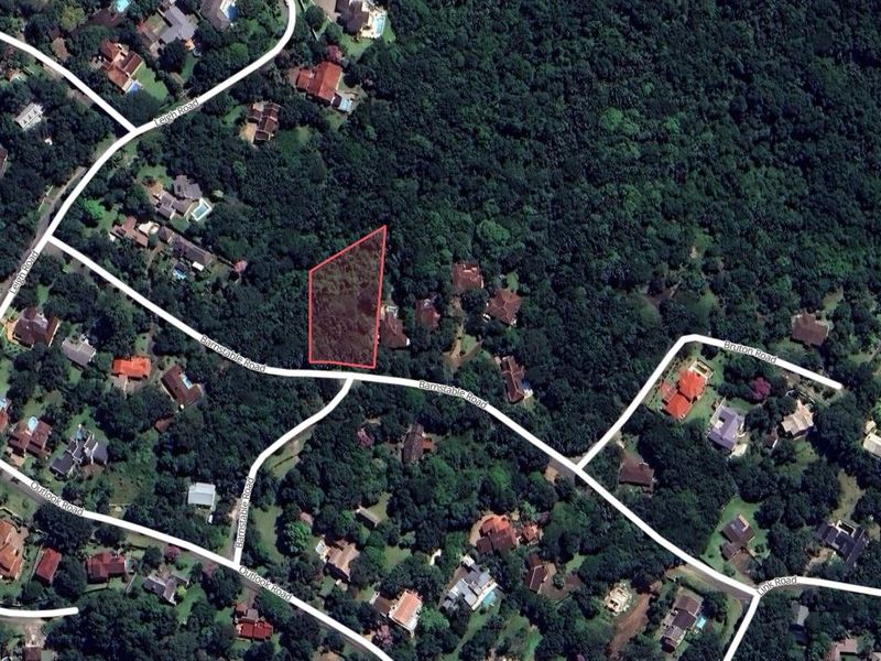 An aerial view showing a vacant residential plot surrounded by dense vegetation and established neighborhood roads.