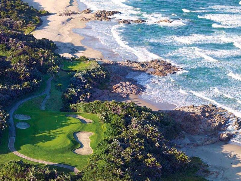 An aerial view of a coastal golf course featuring manicured greens, sand bunkers, and direct access to the rocky shoreline and ocean.