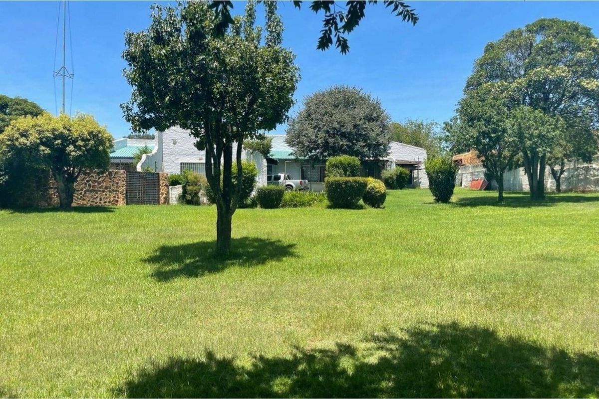 A spacious rear garden featuring a large lawn, mature trees, and a stone boundary wall, providing a private outdoor setting.