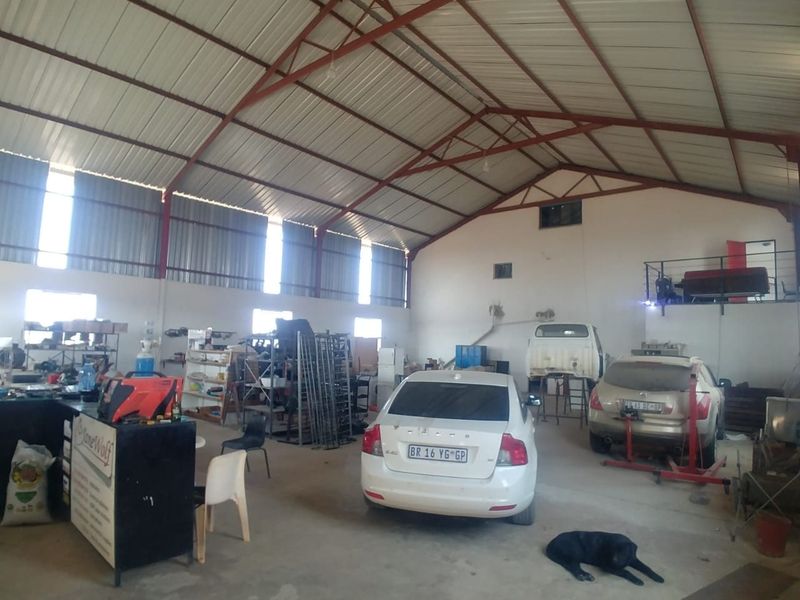 Large industrial-style garage space featuring high exposed steel roof trusses, concrete flooring, and a mezzanine level, suitable for workshop or storage use.