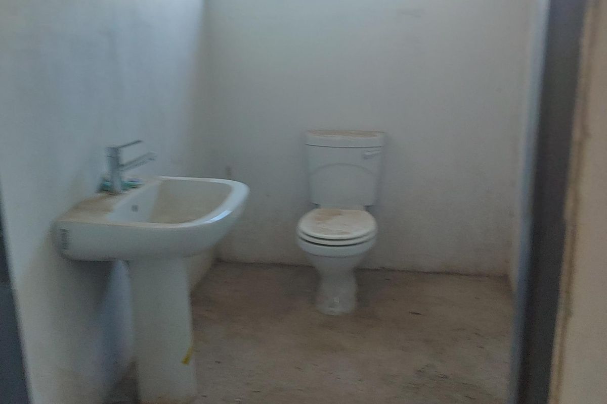 A basic, unfinished bathroom featuring a pedestal basin and toilet, requiring flooring and cosmetic updates to improve functionality and aesthetic appeal.