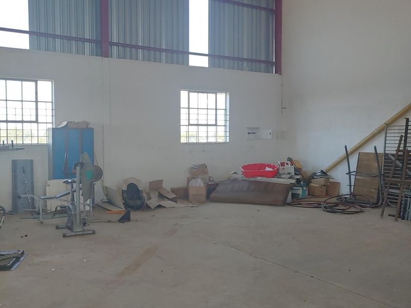 A large, open-plan utility or storage space featuring exposed steel roof trusses, corrugated metal cladding, and concrete flooring, suitable for workshop or storage use.