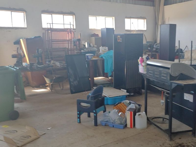 A spacious, unfinished garage or utility area featuring concrete flooring, exposed steel roof trusses, and high-level windows, suitable for storage or workshop use.