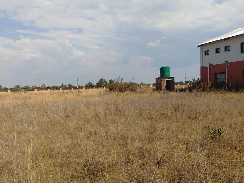 A view of the rear property grounds featuring an overgrown field, a water storage tank, and the side elevation of the main building structure.