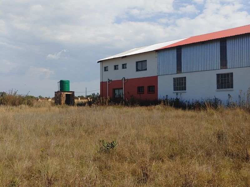 Rear view of a large industrial-style building featuring a metal roof, exterior water tank, and expansive surrounding land.