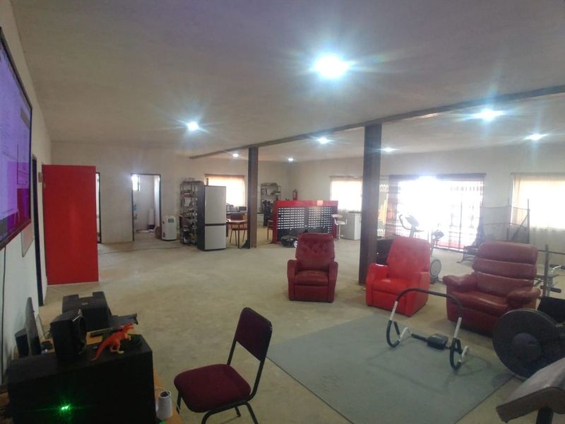 A large, open-plan living space featuring structural support columns and recessed lighting, currently utilized as a multi-purpose area with unfinished concrete flooring.