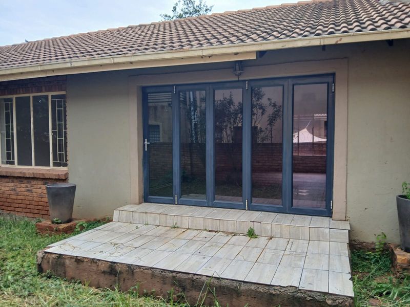 Rear exterior view featuring a tiled patio area with modern aluminium folding doors and a brick and plaster facade.