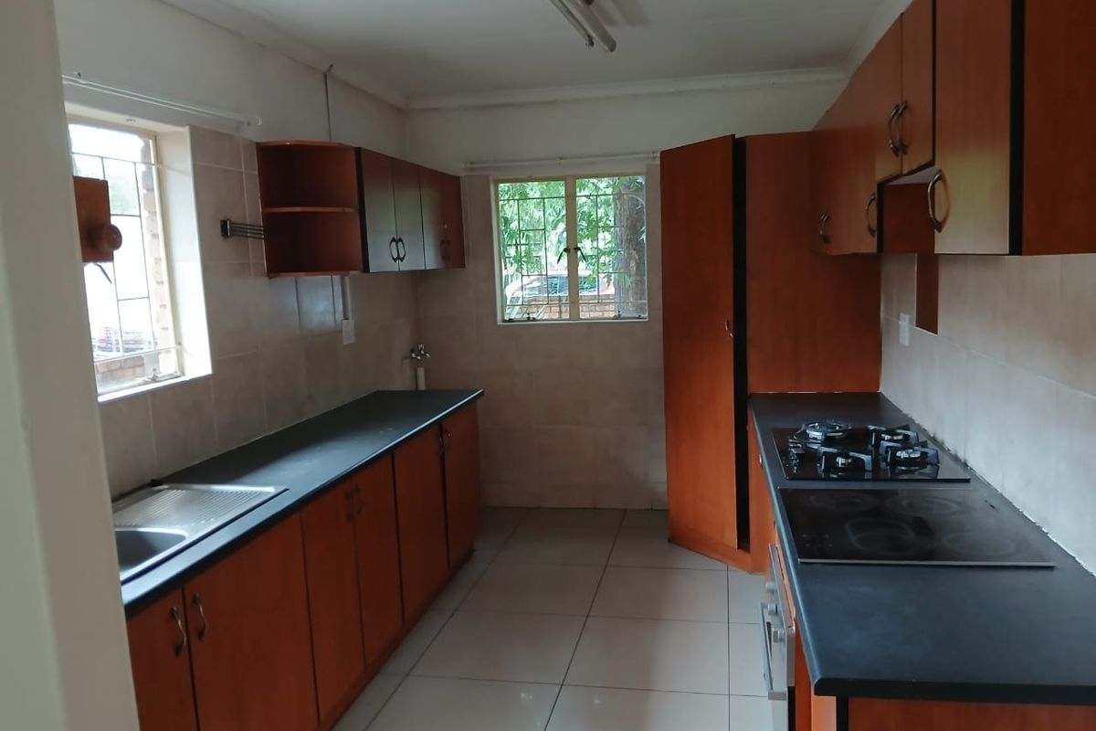 A functional kitchen featuring wooden cabinetry, dark countertops, dual hobs, and tiled flooring, offering a practical layout ready for modernization.