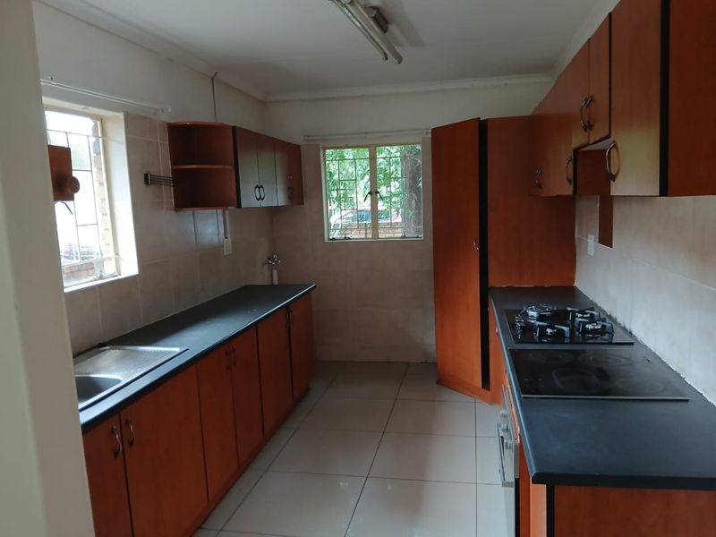 A functional kitchen featuring wooden cabinetry, dark countertops, dual hobs, and tiled flooring, offering a practical layout ready for modernization.