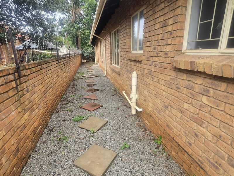 A side exterior pathway featuring a gravel surface with stone pavers, bordered by a brick wall and the side elevation of the house.