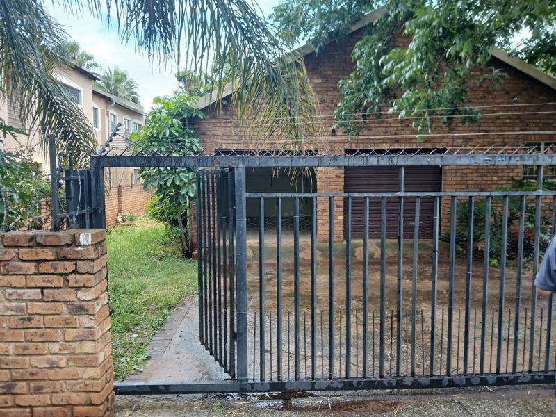 Front view of a brick house featuring a double garage with roller shutter doors, secured by a metal gate and electric fencing.