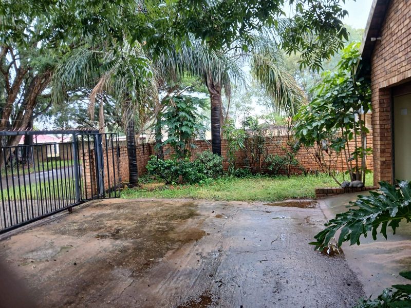 Front exterior area featuring a concrete driveway, metal gate, and brick boundary wall with established garden landscaping.