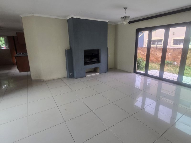 Spacious, empty living room featuring large format floor tiles, a central built-in fireplace, and sliding glass doors providing access to the rear garden.