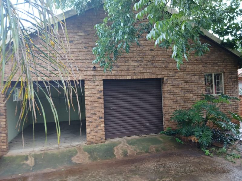 A detached face brick garage featuring one roller shutter door and an additional open parking bay, set on a concrete driveway.