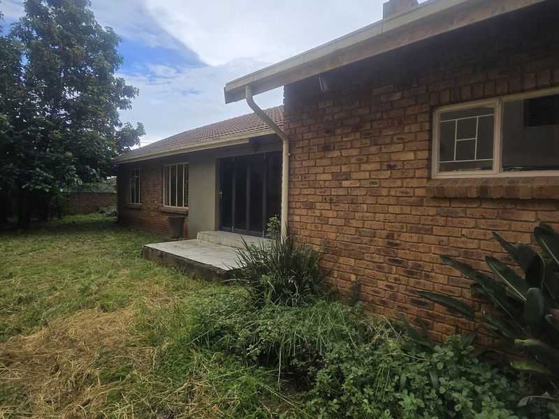 Rear view of the house featuring a brick facade, tiled roof, and a small concrete patio area accessible via sliding glass doors.