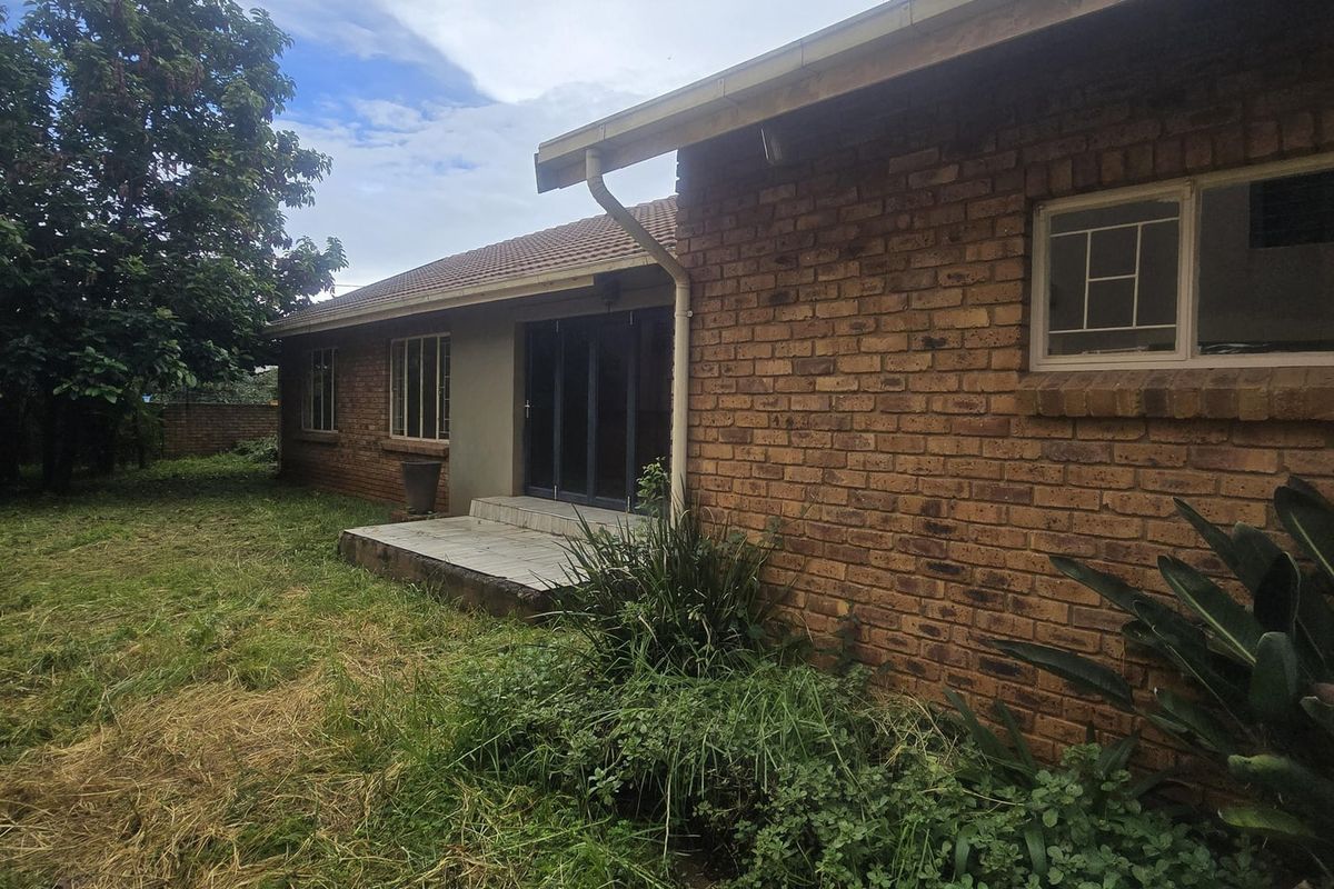 Rear view of the house featuring a brick facade, tiled roof, and a small concrete patio area accessible via sliding glass doors.