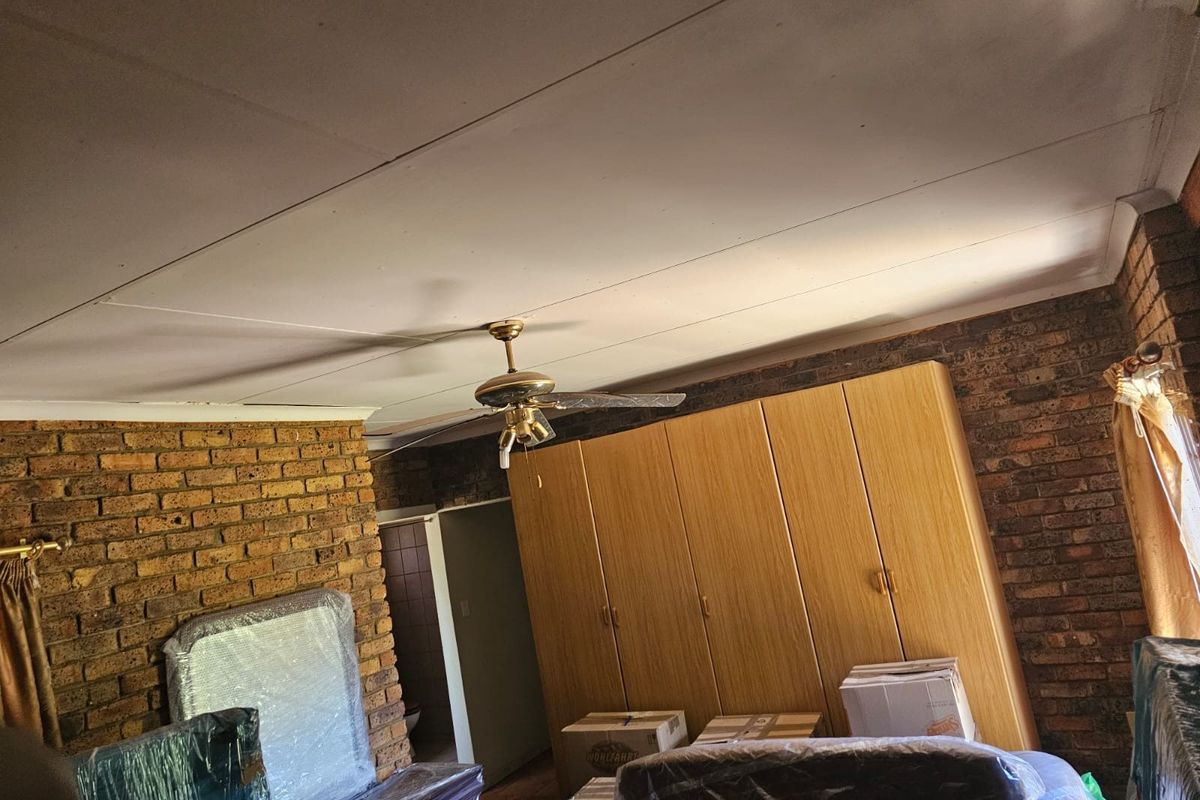 Bedroom featuring exposed brick walls, built-in wooden cupboards, and a ceiling fan. The room requires ceiling repairs and cosmetic updates.