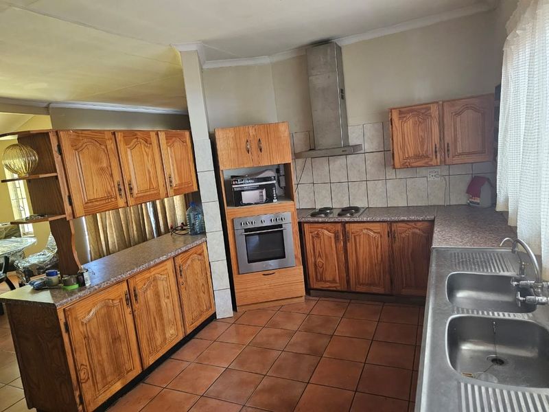 A functional kitchen featuring wooden cabinetry, laminate countertops, a built-in oven with hob, and a stainless steel double sink with tiled backsplash.