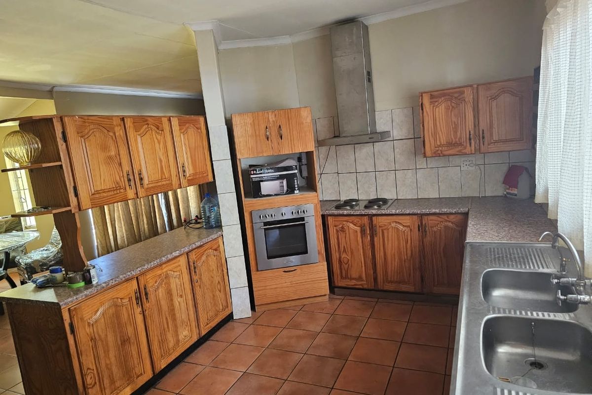A functional kitchen featuring wooden cabinetry, laminate countertops, a built-in oven with hob, and a stainless steel double sink with tiled backsplash.