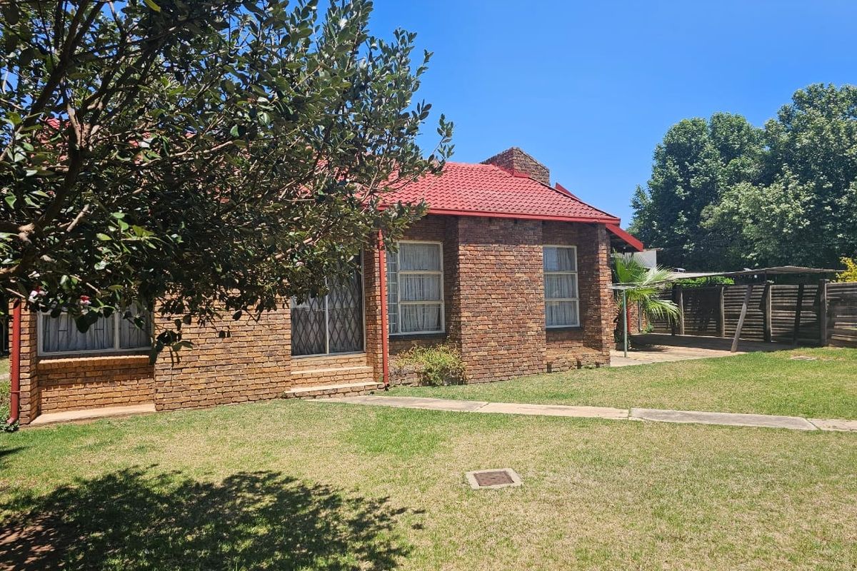 A rear view of a face brick house featuring a red tiled roof, a well-maintained lawn, and a paved walkway leading to the entrance.