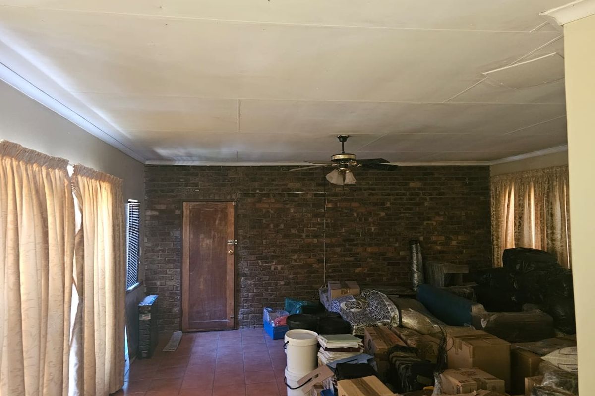 A living room featuring an exposed brick feature wall, tiled flooring, and a ceiling fan, currently cluttered with storage items.
