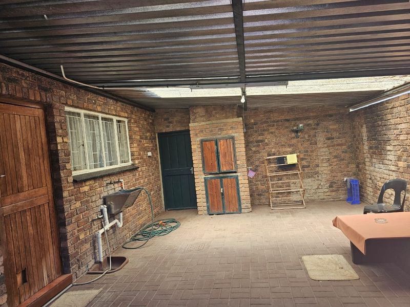 A covered outdoor patio area featuring exposed brick walls, a built-in brick braai, and a utility sink, providing a functional space for outdoor entertaining.