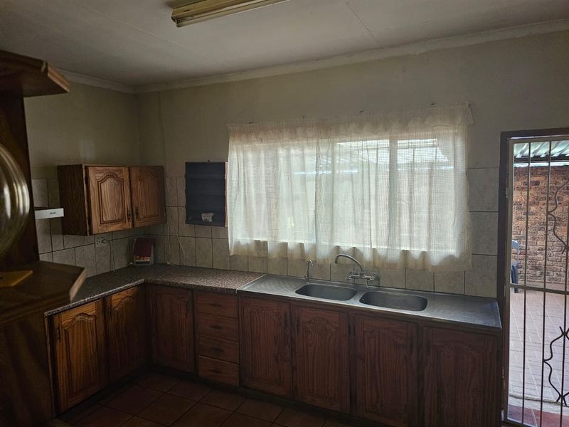 A dated kitchen featuring wooden cabinetry, laminate countertops, and a double bowl stainless steel sink with direct access to an outdoor area.