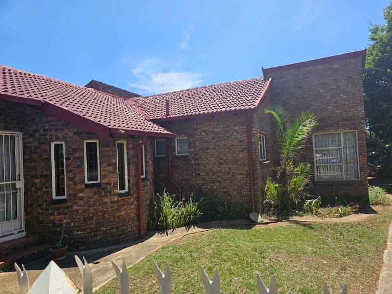 Front elevation of a face brick house featuring a tiled roof, security gate, and established garden area.